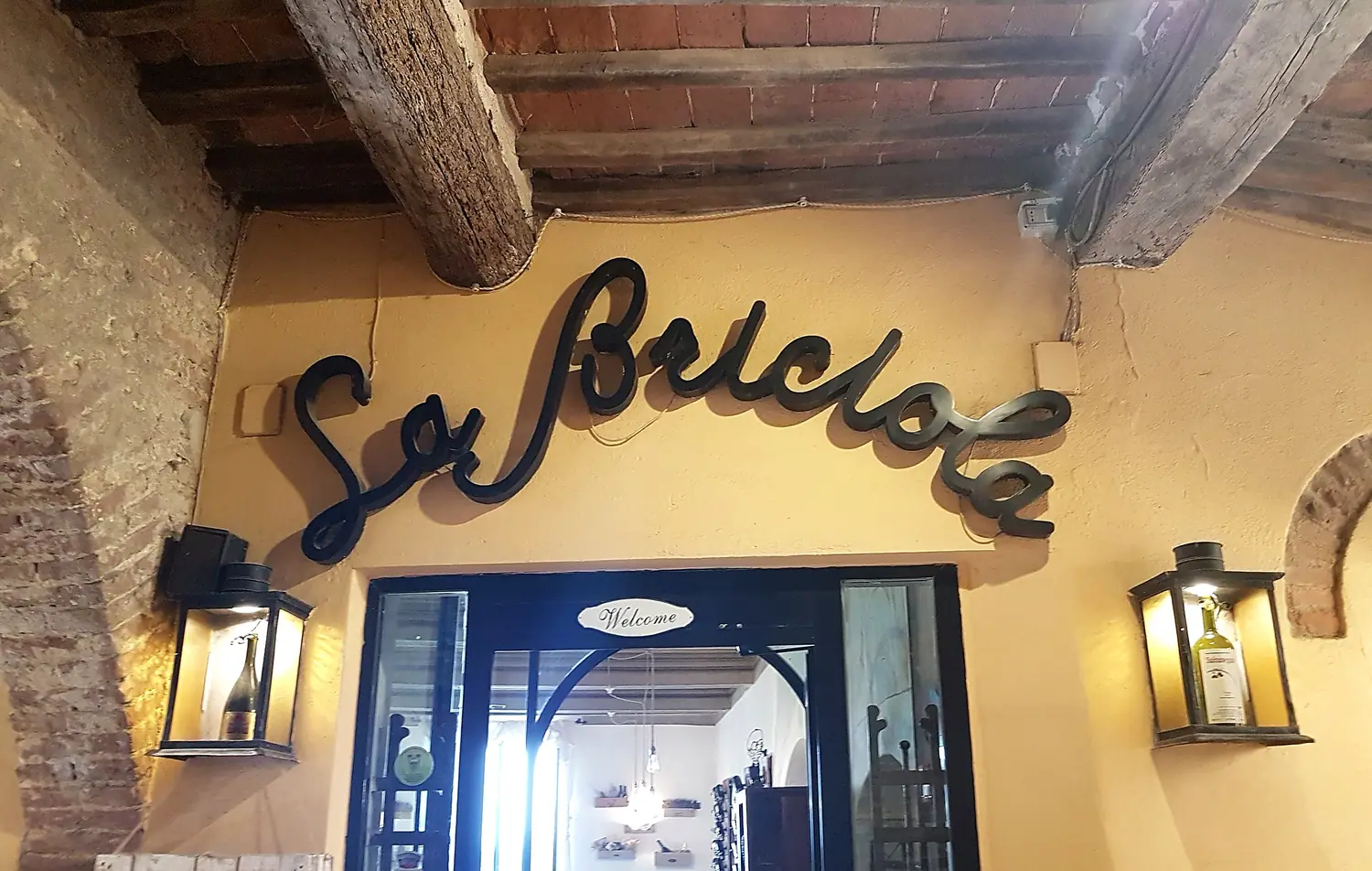 L'ingresso della Briciola: insegna in ferro battuto sul muro ocra, lanterne e la sala illuminata dentro