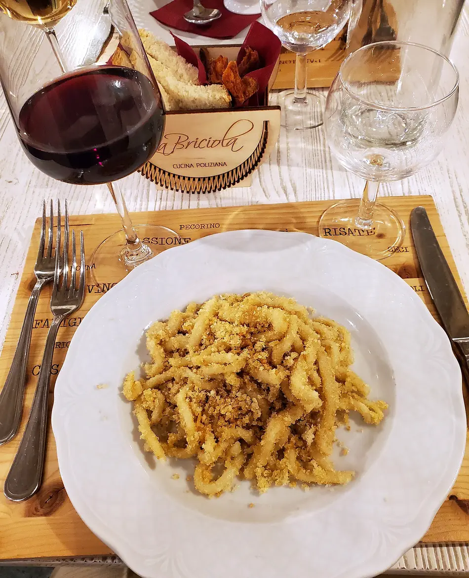 Un piatto di pici alle briciole, con il cestino del pane marchiato e un calice di rosso
