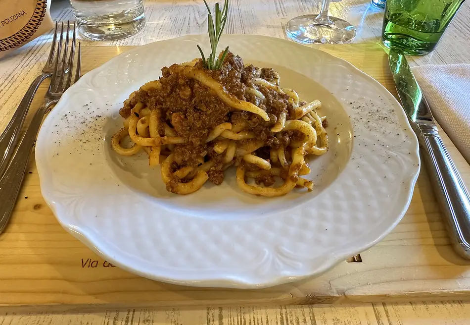 Un piatto di pici al ragù con un rametto di rosmarino, sulla tovaglietta marchiata