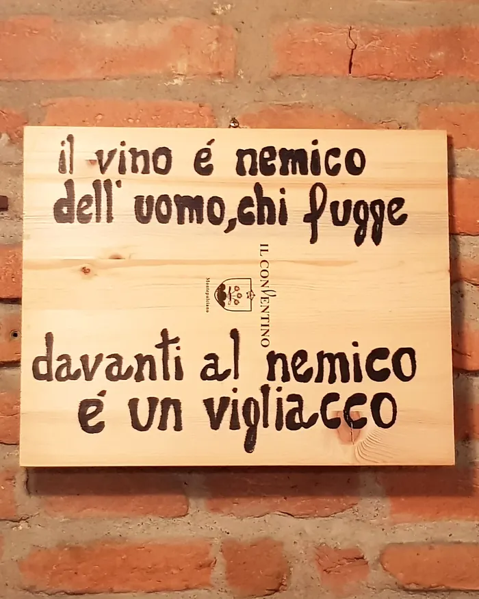 Targa di legno sul muro di mattoni: il vino é nemico dell'uomo, chi fugge davanti al nemico é un vigliacco